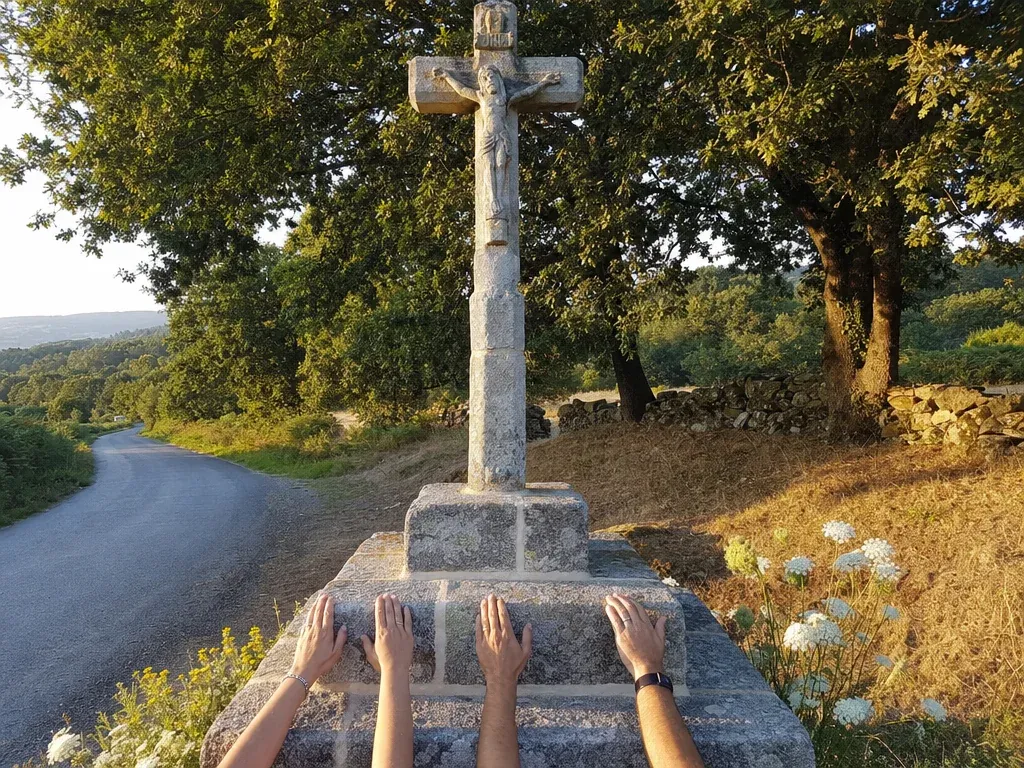 Recreación: el cruceiro de piedra de nuevo en su sitio, junto a una carretera, con tres pares de manos en la base
